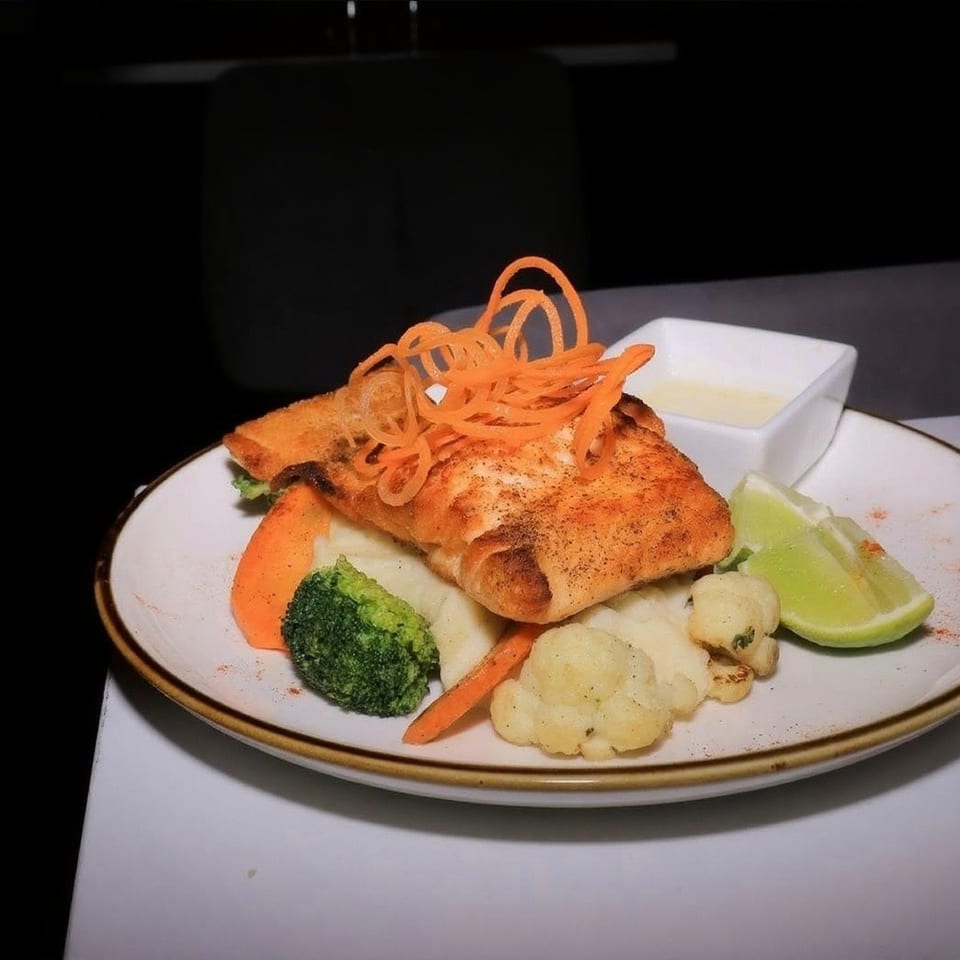 Pan-seared fish with shredded carrots, mashed potatoes, broccoli, cauliflower, and lime on a plate.