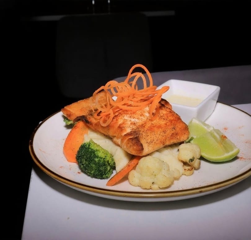 Pan-seared fish with shredded carrots, mashed potatoes, broccoli, cauliflower, and lime on a plate.