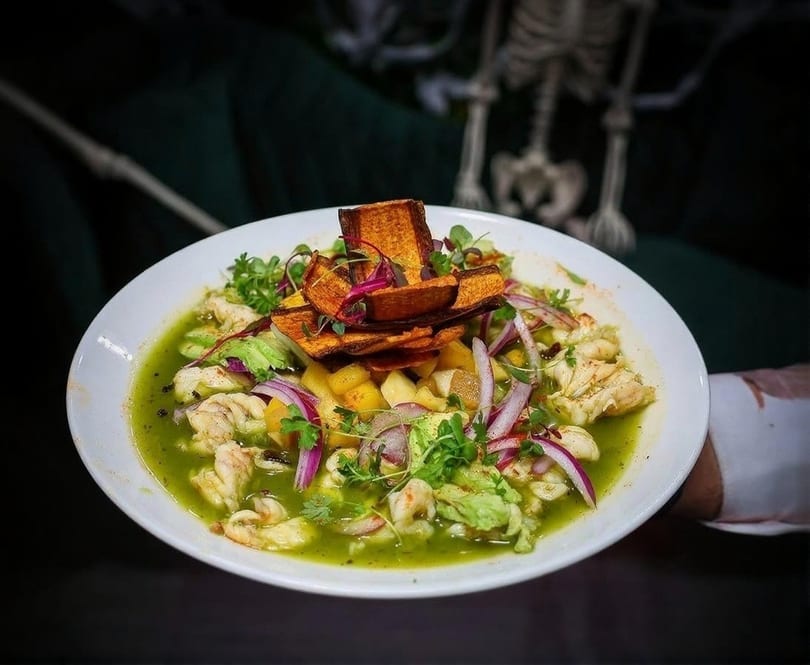 Ceviche with shrimp, red onion, avocado, and sweet potato chips in a green sauce.