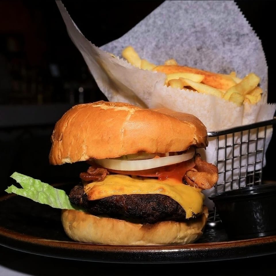 Cheeseburger with lettuce, tomato, onion, bacon, and fries in a metal basket.