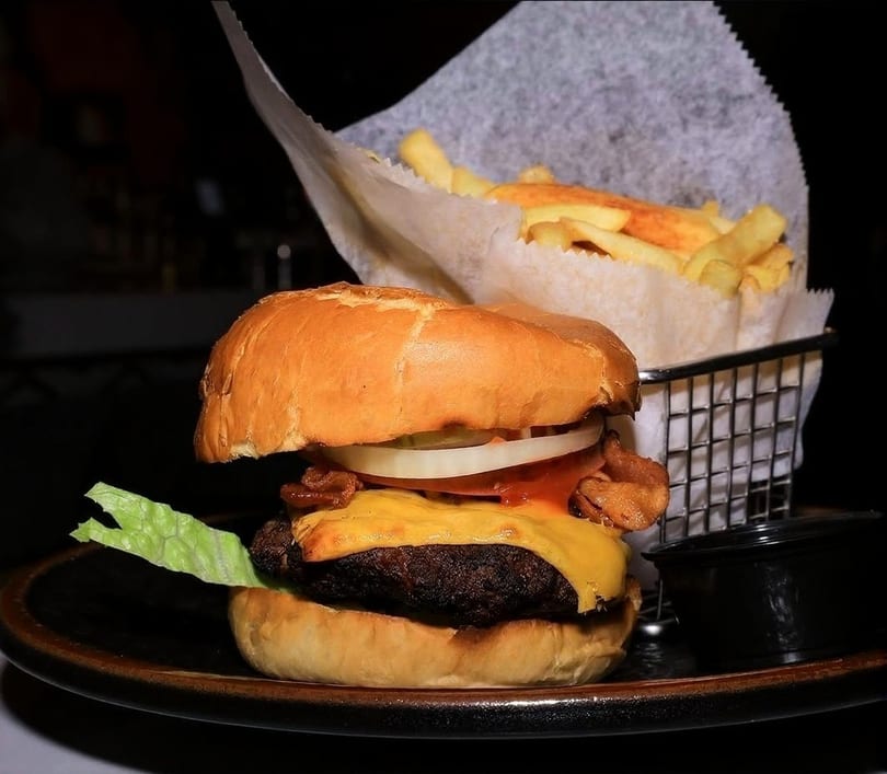 Cheeseburger with lettuce, tomato, onion, bacon, and fries in a metal basket.