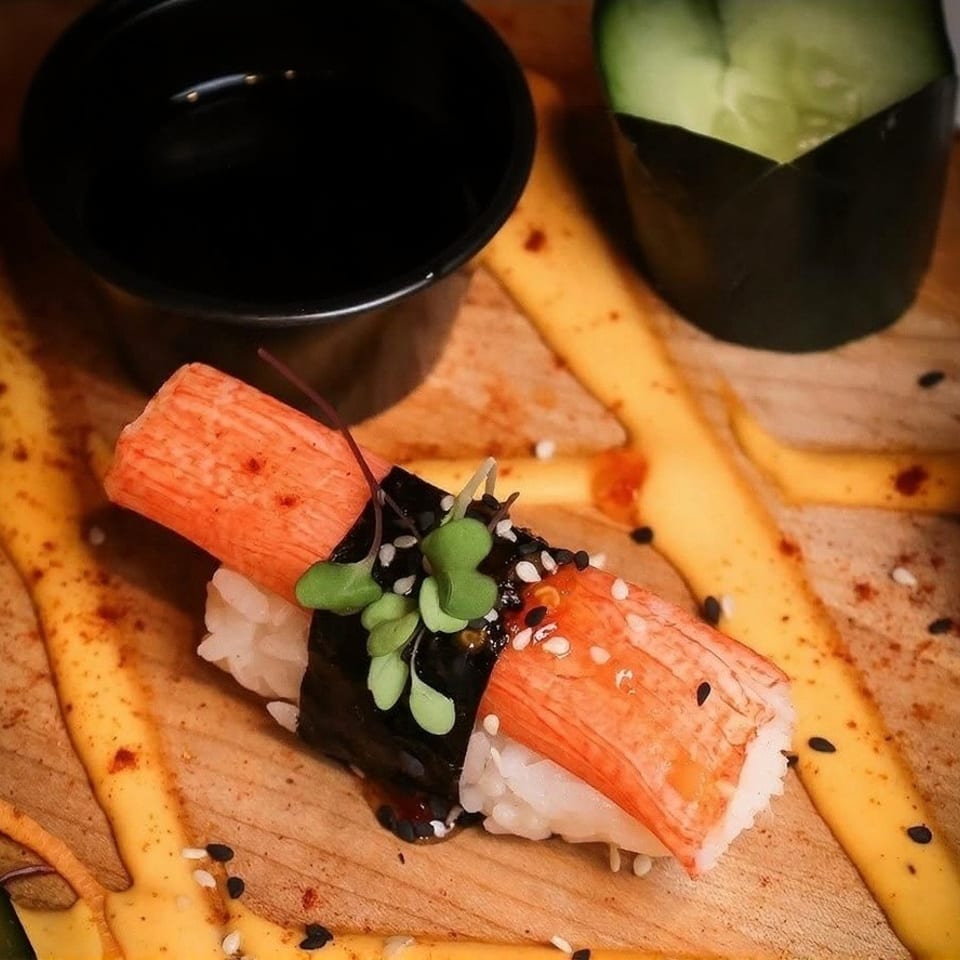 Nigiri sushi with crab stick, seaweed, rice, sesame seeds, and microgreens on a wooden board.