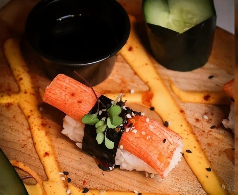 Nigiri sushi with crab stick, seaweed, rice, sesame seeds, and microgreens on a wooden board.