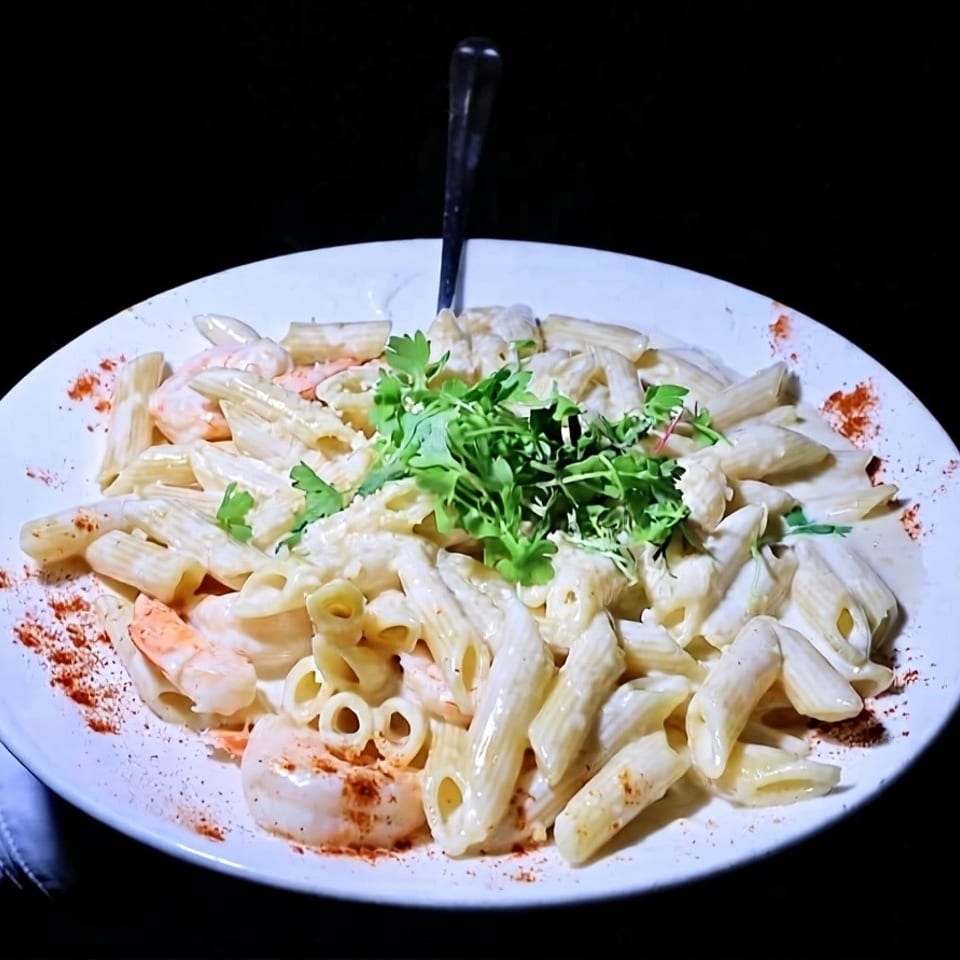 Creamy penne pasta with shrimp, garnished with fresh herbs and paprika, on a white plate.