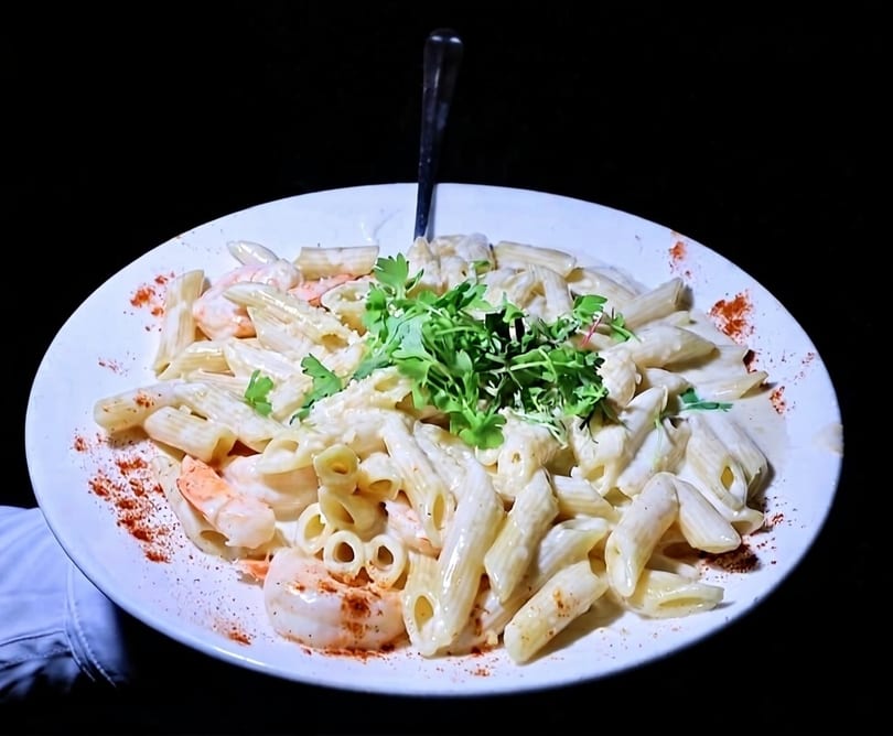 Creamy penne pasta with shrimp, garnished with fresh herbs and paprika, on a white plate.