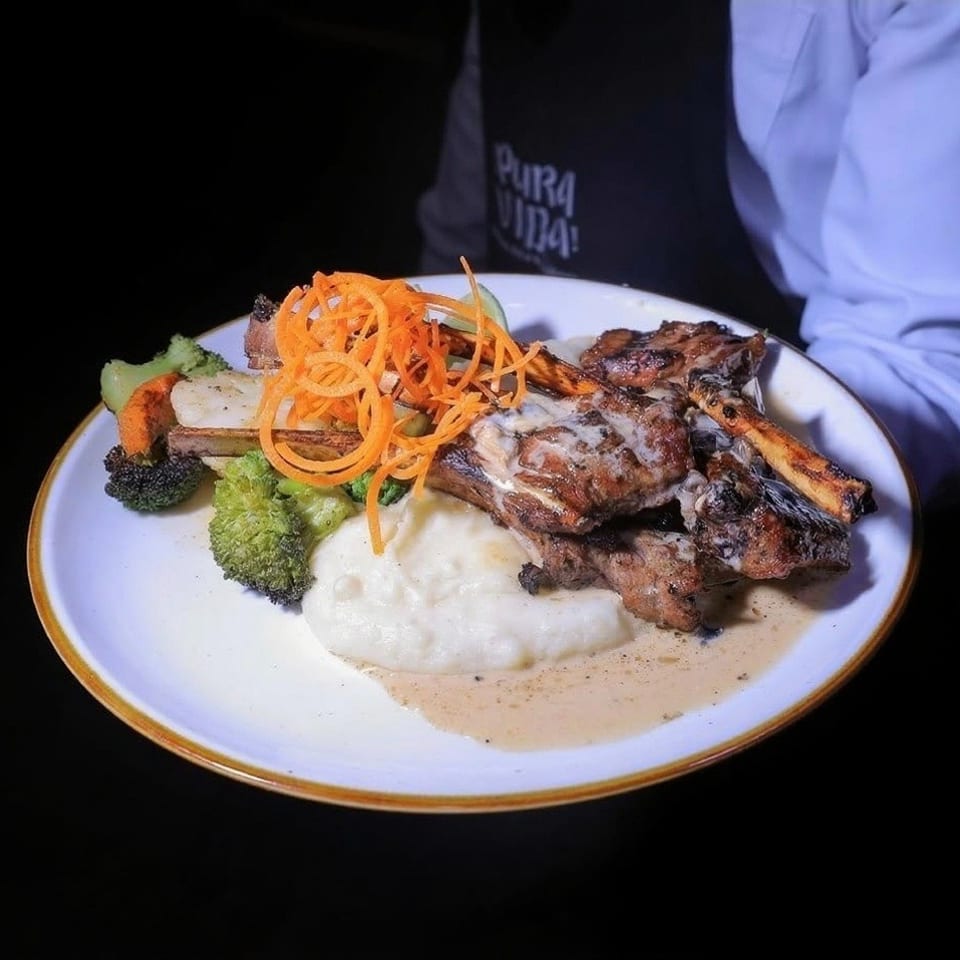 A plate of grilled ribs with mashed potatoes, broccoli, carrots, and a creamy sauce.
