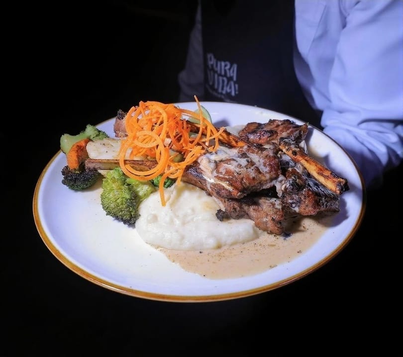 A plate of grilled ribs with mashed potatoes, broccoli, carrots, and a creamy sauce.