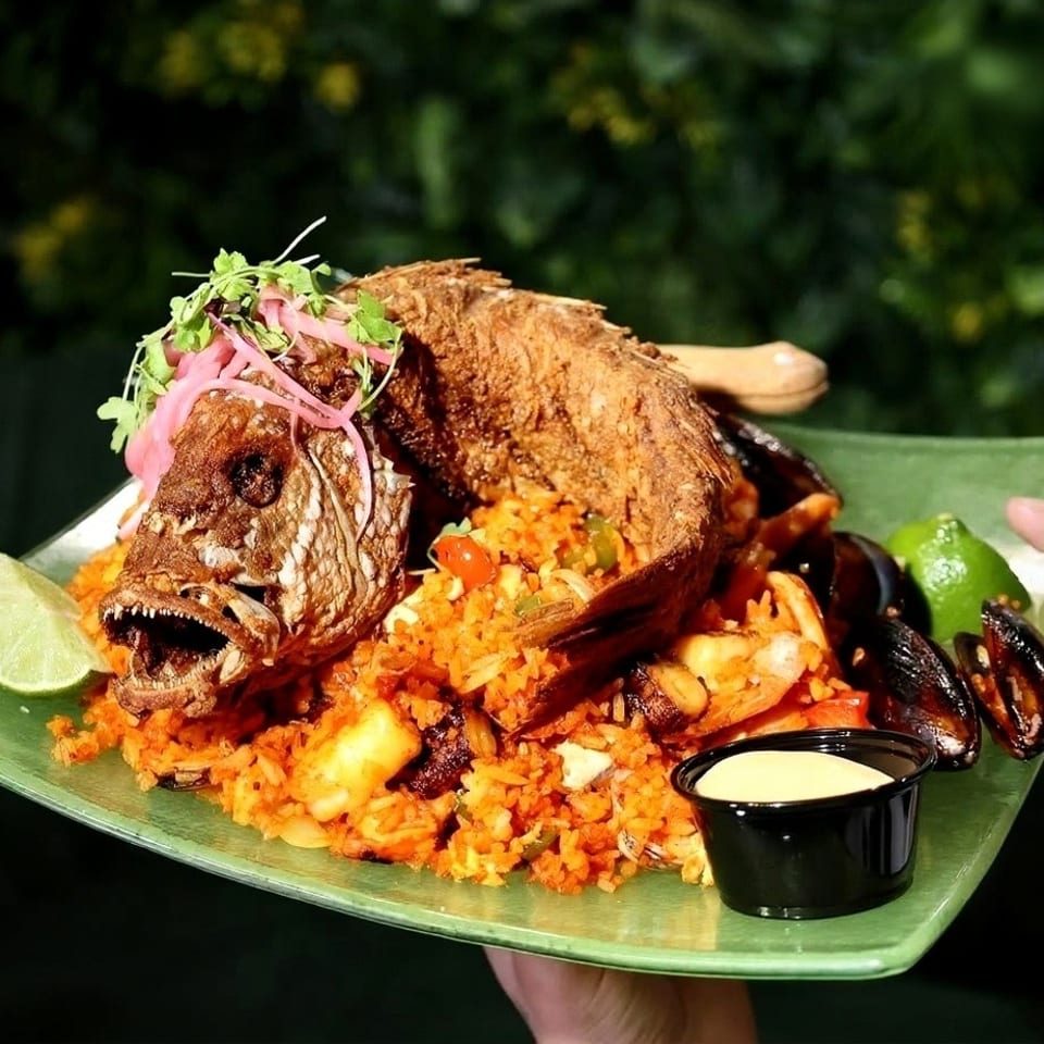 Whole fried fish with rice, mussels, and lime wedges on a green plate.