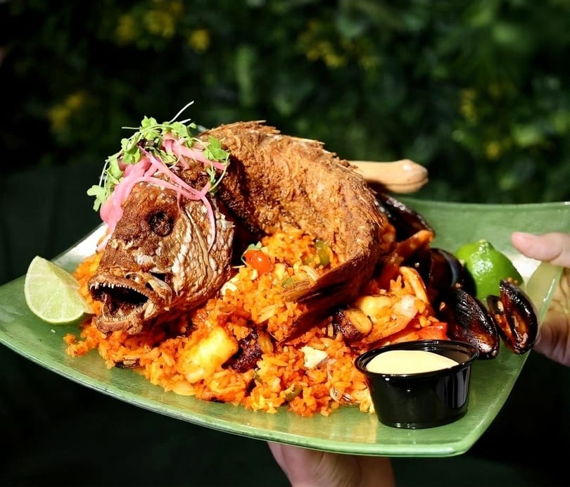 Whole fried fish with rice, mussels, and lime wedges on a green plate.